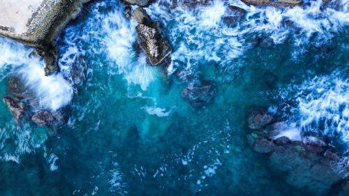 Free Spectacular aerial view of vibrant blue waves crashing over rocky coastline, creating dramatic and dynamic ocean scene. Stock Photo