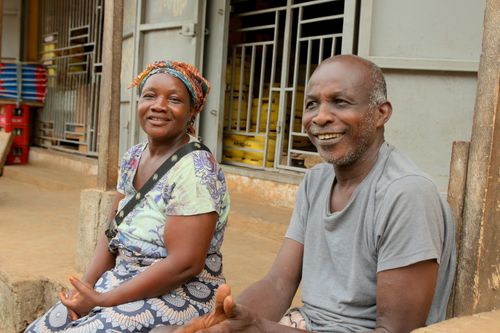 Free A cheerful couple sitting outside a shop in Freetown, Sierra Leone, enjoying a conversation. Stock Photo