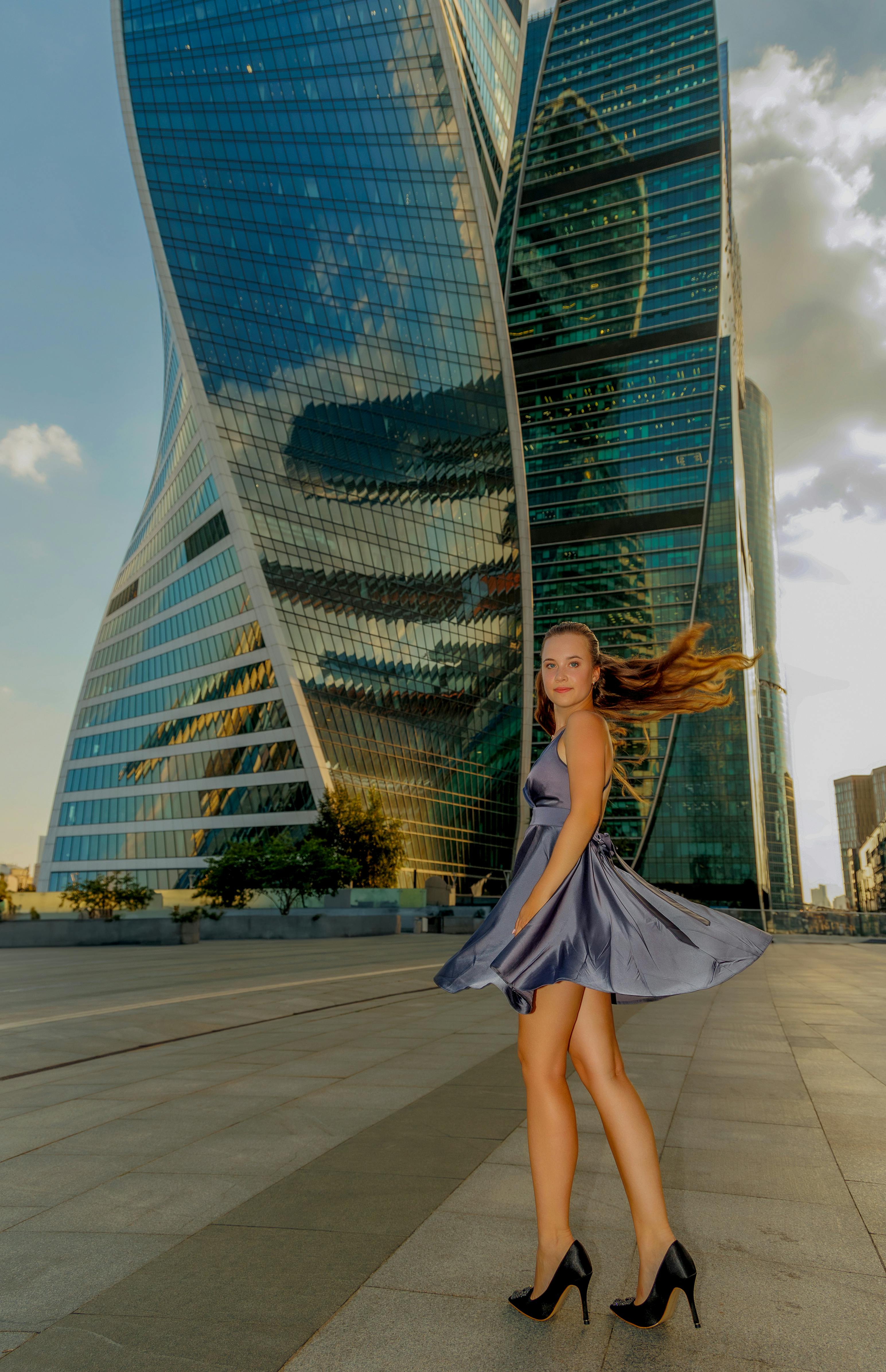 Free Model in elegant dress poses by a twisting skyscraper, showcasing urban style. Stock Photo