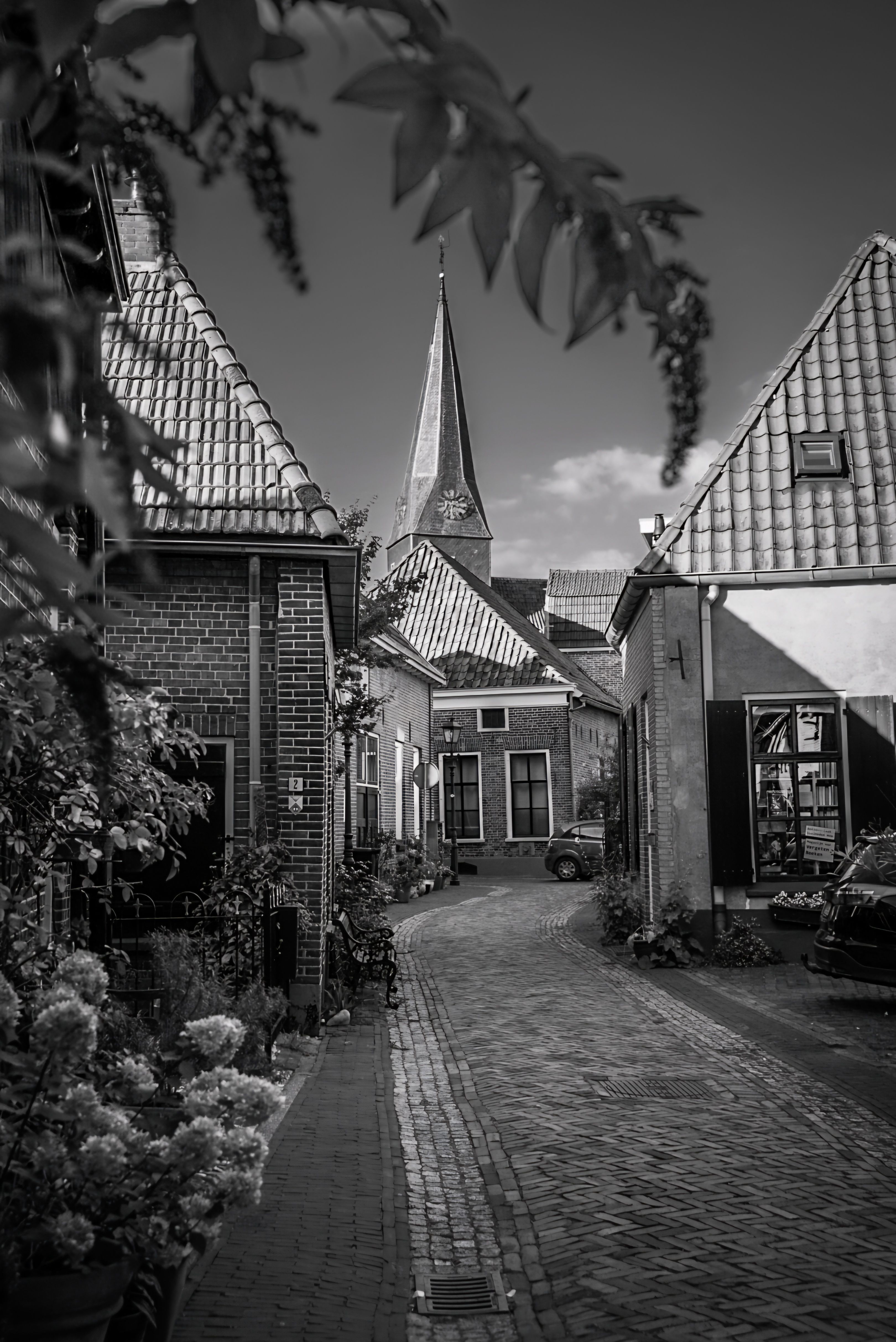 Black and white photo of a European cobblestone street with quaint houses and a church steeple.