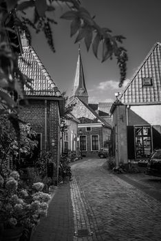 Black and white photo of a European cobblestone street with quaint houses and a church steeple.