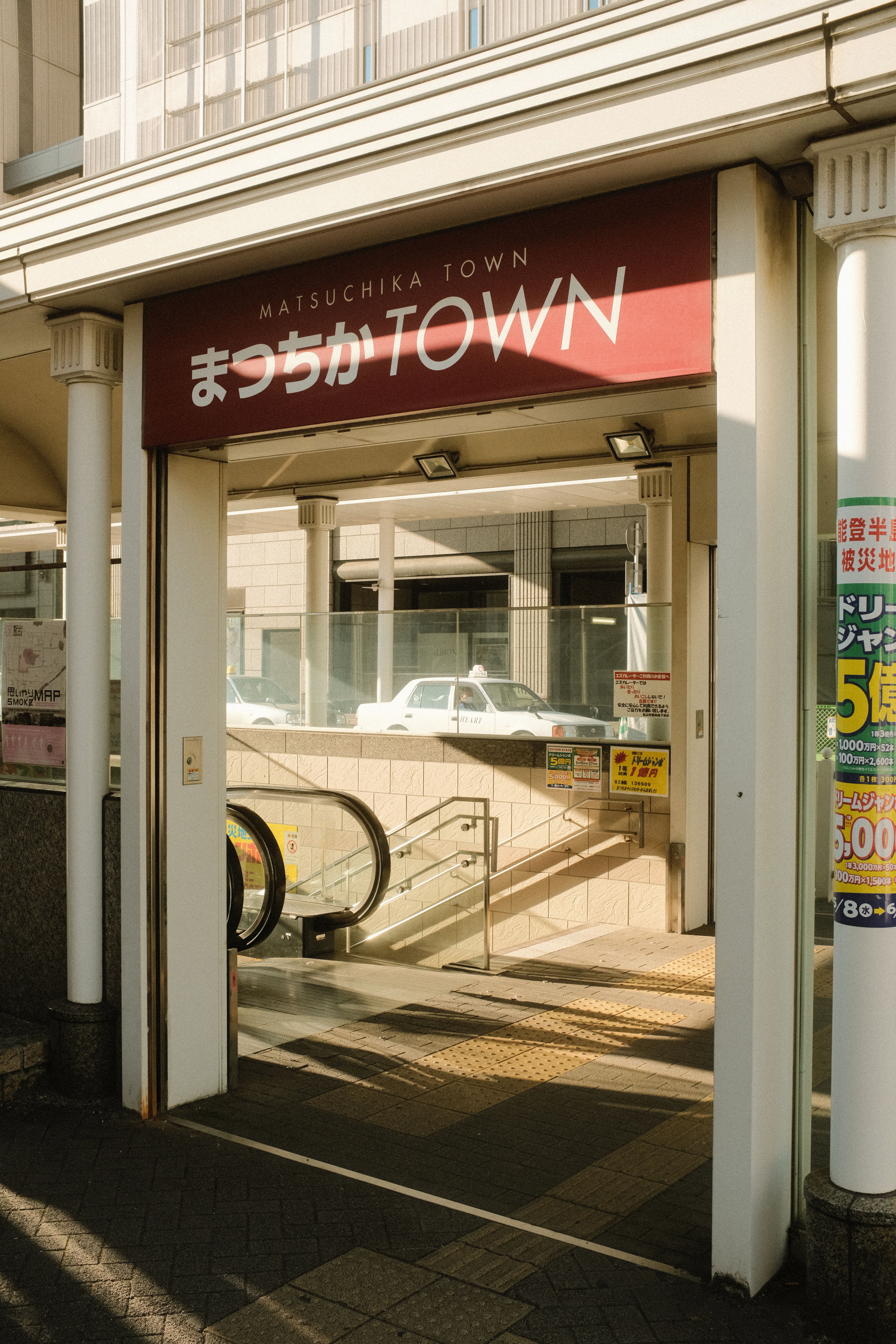 Entrance to Matsuchika Town in Matsuyama, Japan. Sunlit modern shopping area with escalator.