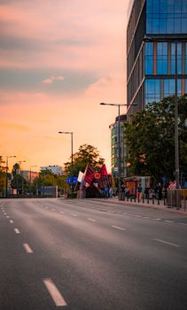 A vibrant city street in Warsaw during sunrise, featuring modern buildings and an empty road.
