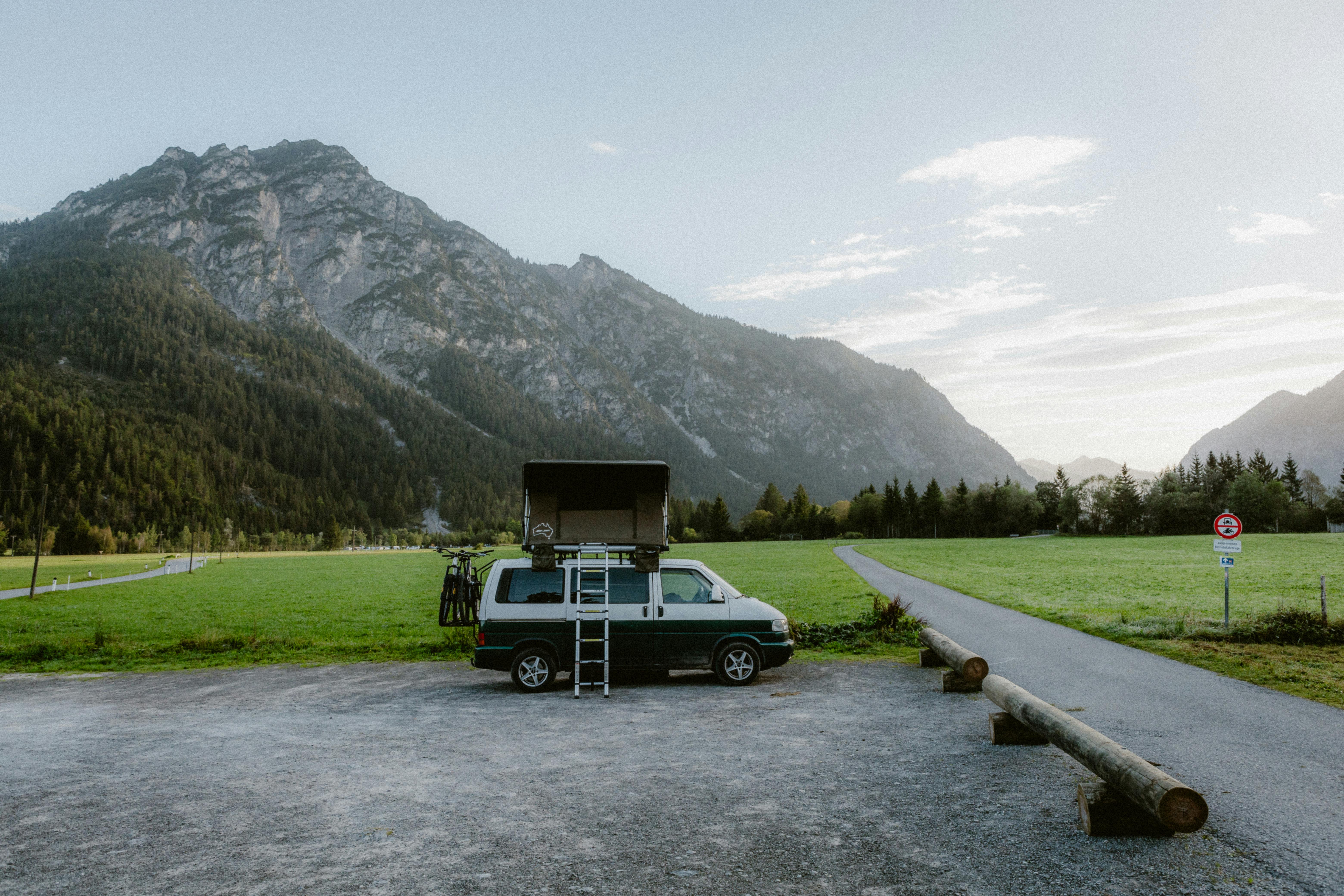 Campervan with rooftop tent parked by rural road, mountains in background.