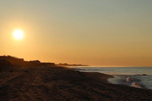 Free A tranquil view of Nantucket beach with golden sunrise over the ocean and coastline. Stock Photo