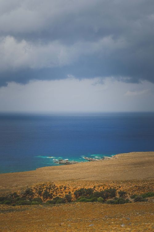Free Moody seascape with horizon and storm clouds over rugged coastline. Perfect for travel or nature themes. Stock Photo