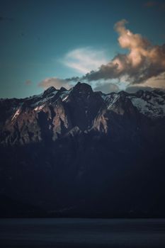 A breathtaking view of shadowed mountains under a twilight sky with clouds.