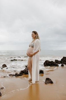 Pregnant woman in a bikini smiling and enjoying the beach, exuding joy and serenity.