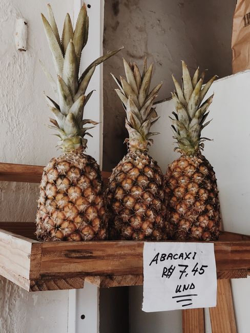 Close-up of ripe pineapples on a wooden shelf with a price tag.