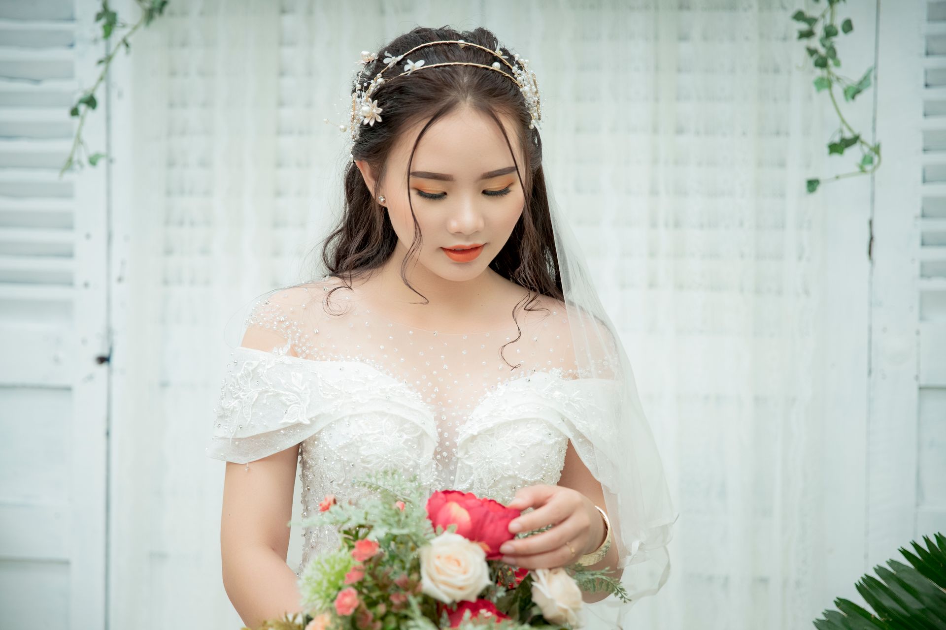 Bride in a lace wedding gown holding a vibrant bouquet indoors.