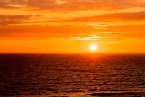 Free Stunning vibrant sunset over the ocean with glowing orange sky and calm sea. Ideal for serene beach atmospheres. Stock Photo