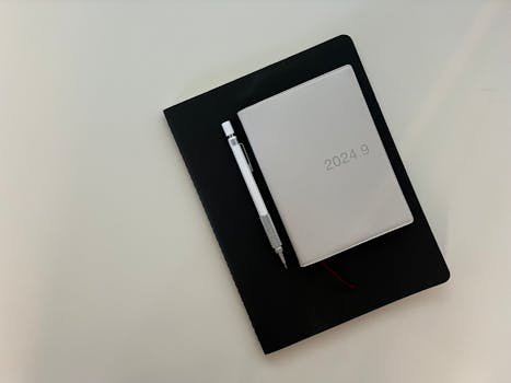 Flat lay of a notebook with a pen and planner on a white table.