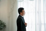 一位身着正式西装的年轻人站在窗边，显得优雅而有风度