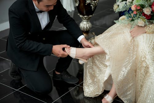 Man in Tuxedo Putting White Sandal on Sitting Woman