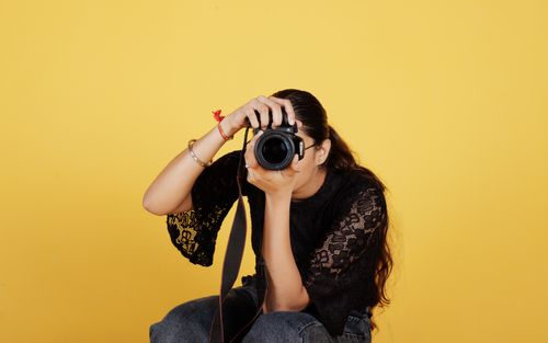 Free A young female photographer taking a photo with a DSLR camera against a yellow background. Stock Photo