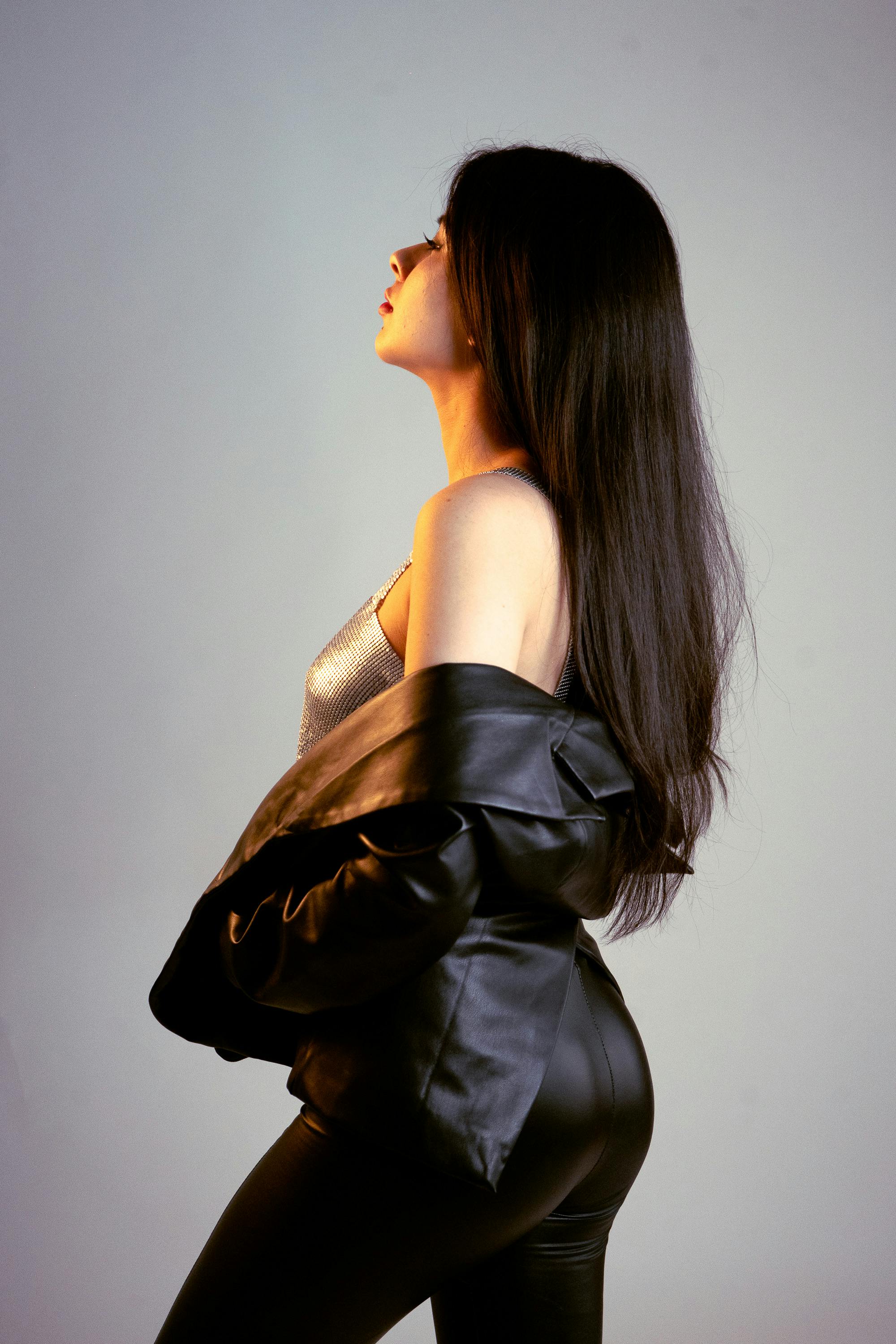 Side view of a woman in a leather jacket and metallic top posing confidently.