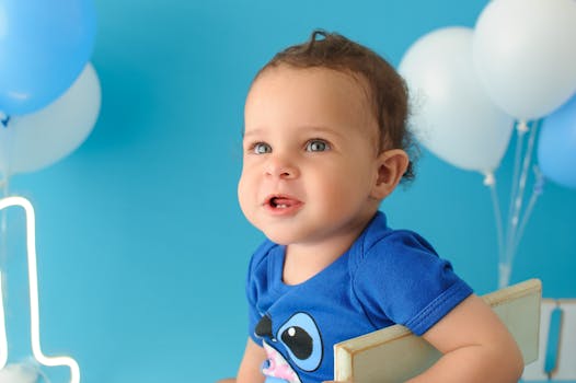 Cheerful baby in blue shirt enjoying first birthday with balloons in a studio shoot.