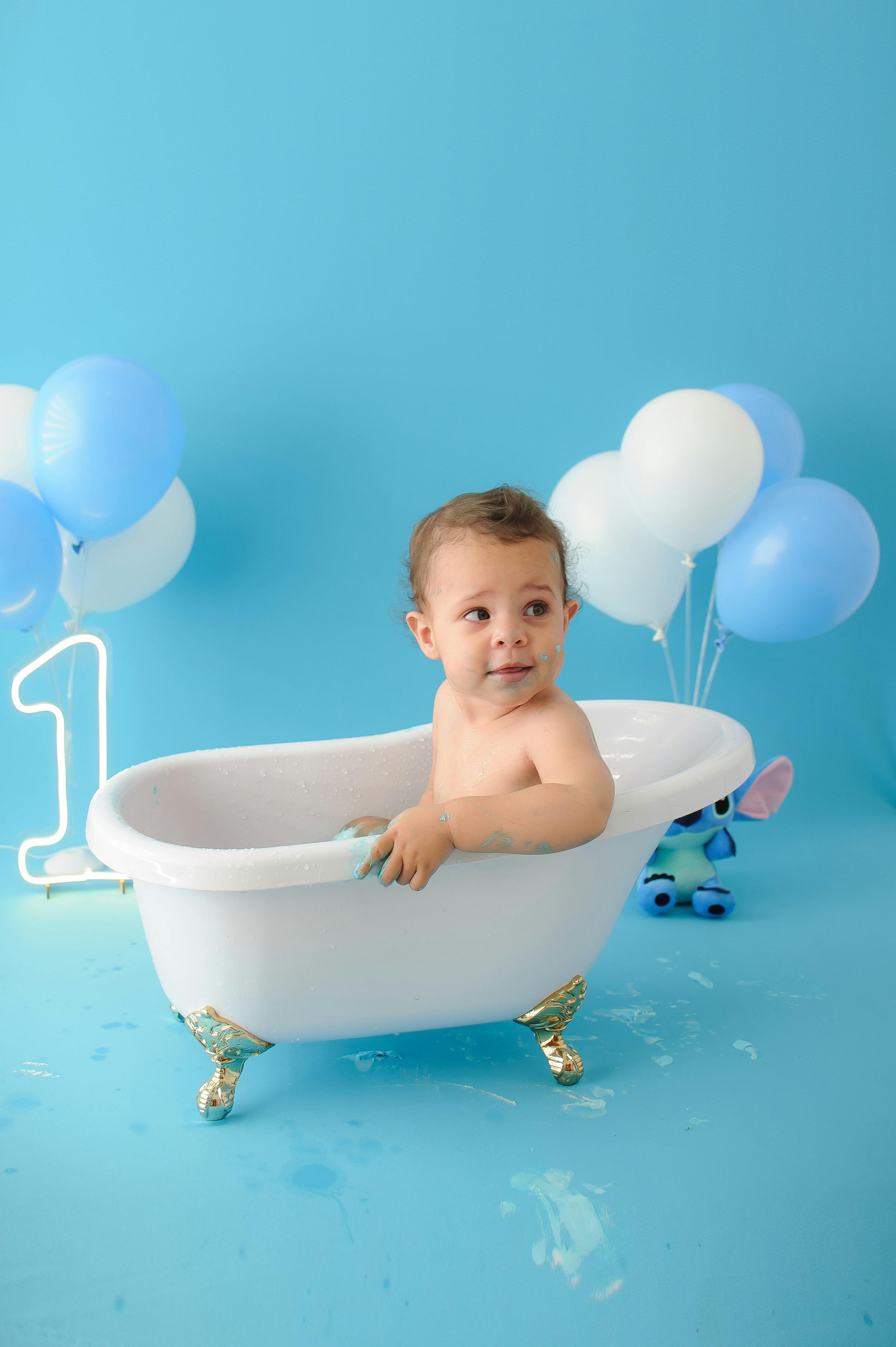 Adorable child in tub with balloons celebrating first birthday in a studio setting.
