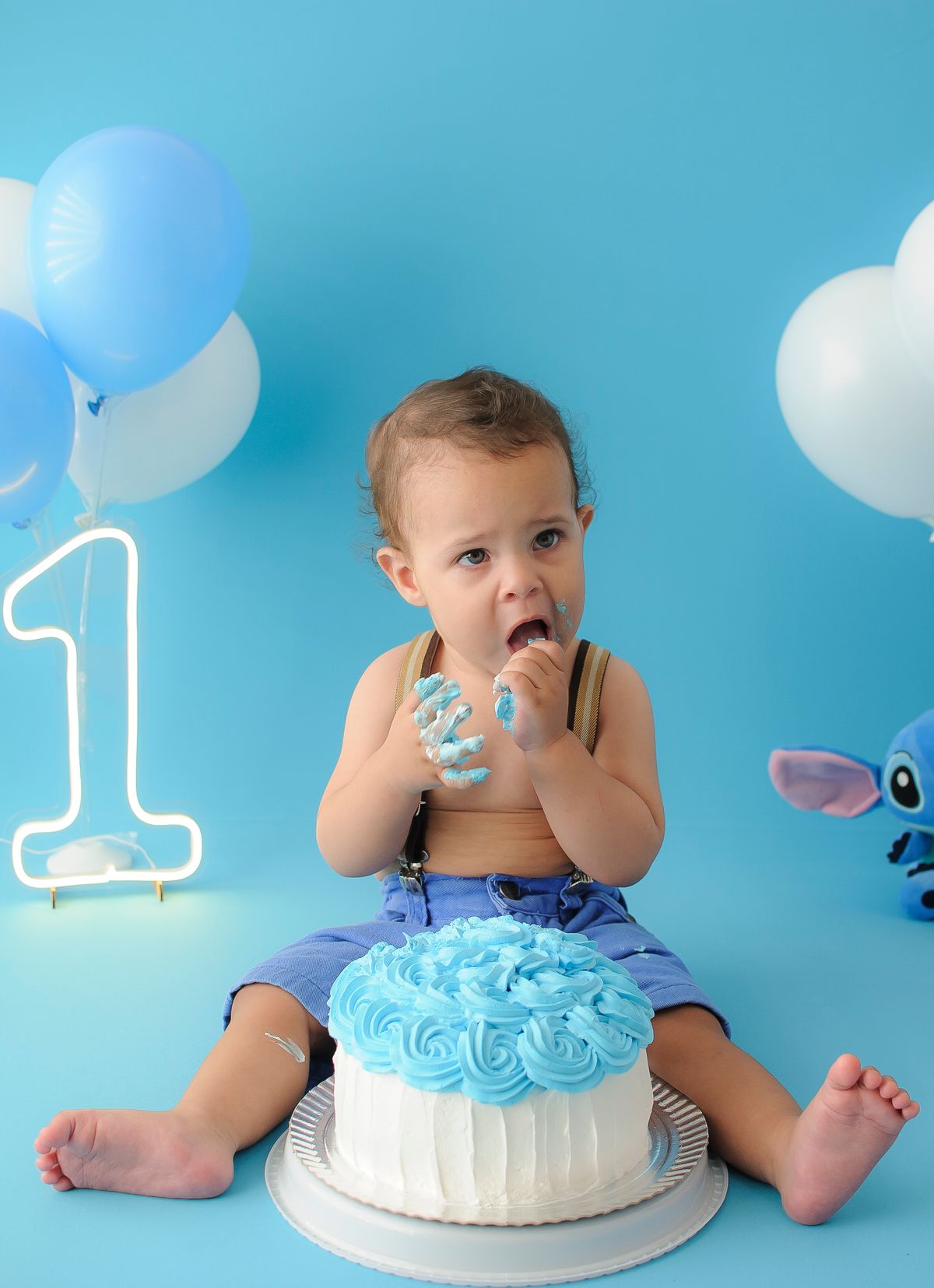 Baby with a blue first birthday smash cake and balloons