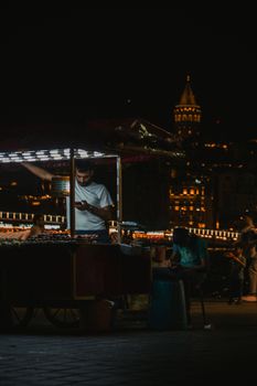 Captivating night scene of a street vendor near Istanbul's iconic Galata Tower with vibrant city lights.