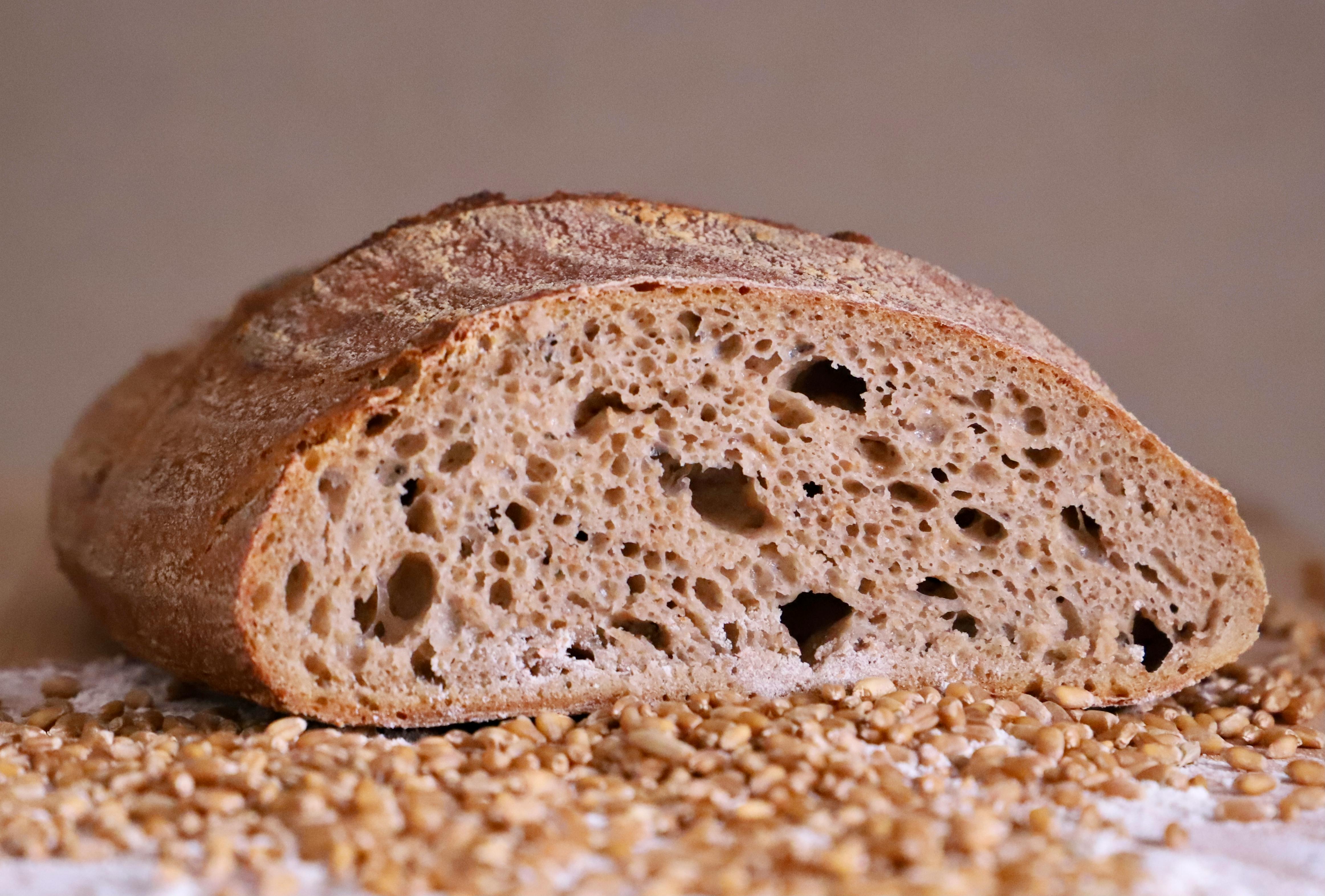 Close-up of a rustic whole grain bread loaf with scattered wheat seeds, highlighting its porous texture.