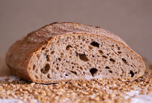 Free Close-up of a rustic whole grain bread loaf with scattered wheat seeds, highlighting its porous texture. Stock Photo