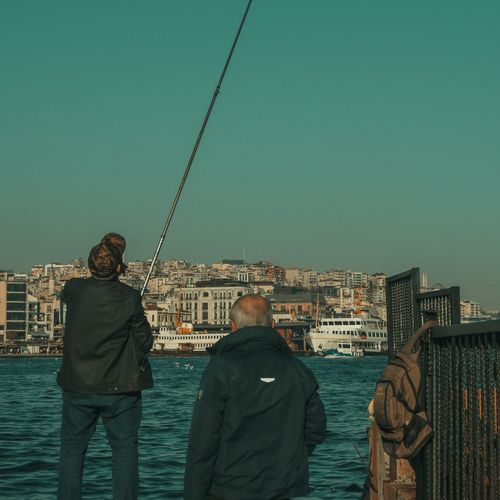 Free Men fishing at the scenic Istanbul harbor with a view of the city in the background. Stock Photo