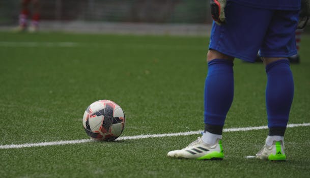 Close-up of a football player standing by a ball during a game on a grass pitch.