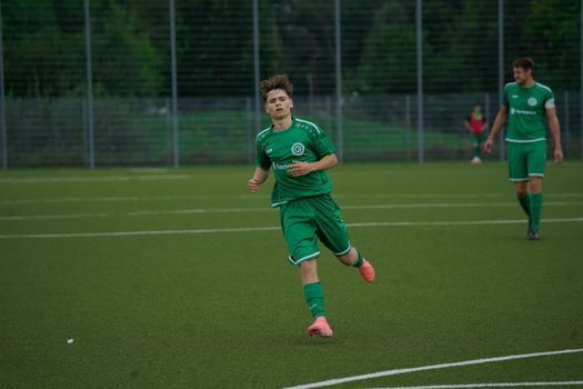 A football player in a green jersey running during an outdoor match on a grass pitch.