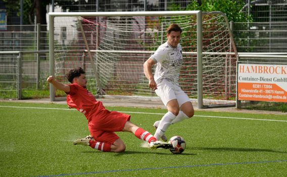 Two footballers in a dynamic sliding tackle on a sunny day during an exciting soccer match.