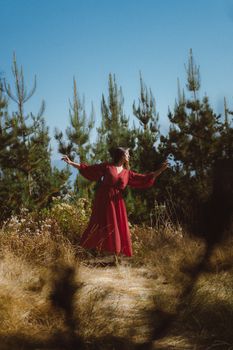 A woman in a red dress poses gracefully among pine trees under a clear blue sky in Lima, Peru.