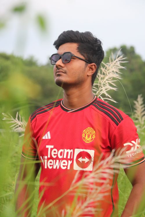 Free Stylish young man in glasses wearing a red sports jersey in lush outdoor setting. Stock Photo