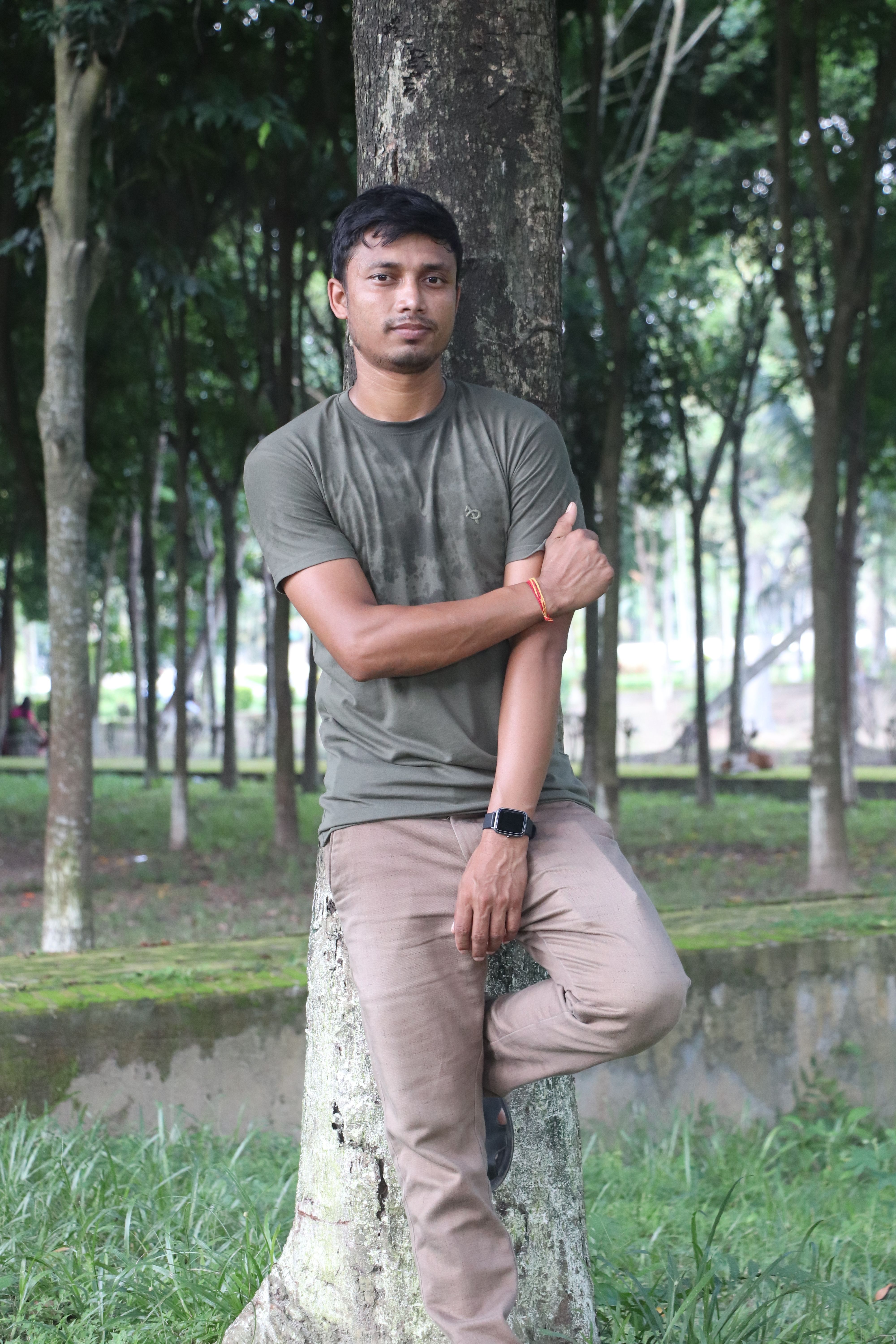 Portrait of a young man standing by a tree in a lush park in Rangpur, Bangladesh.