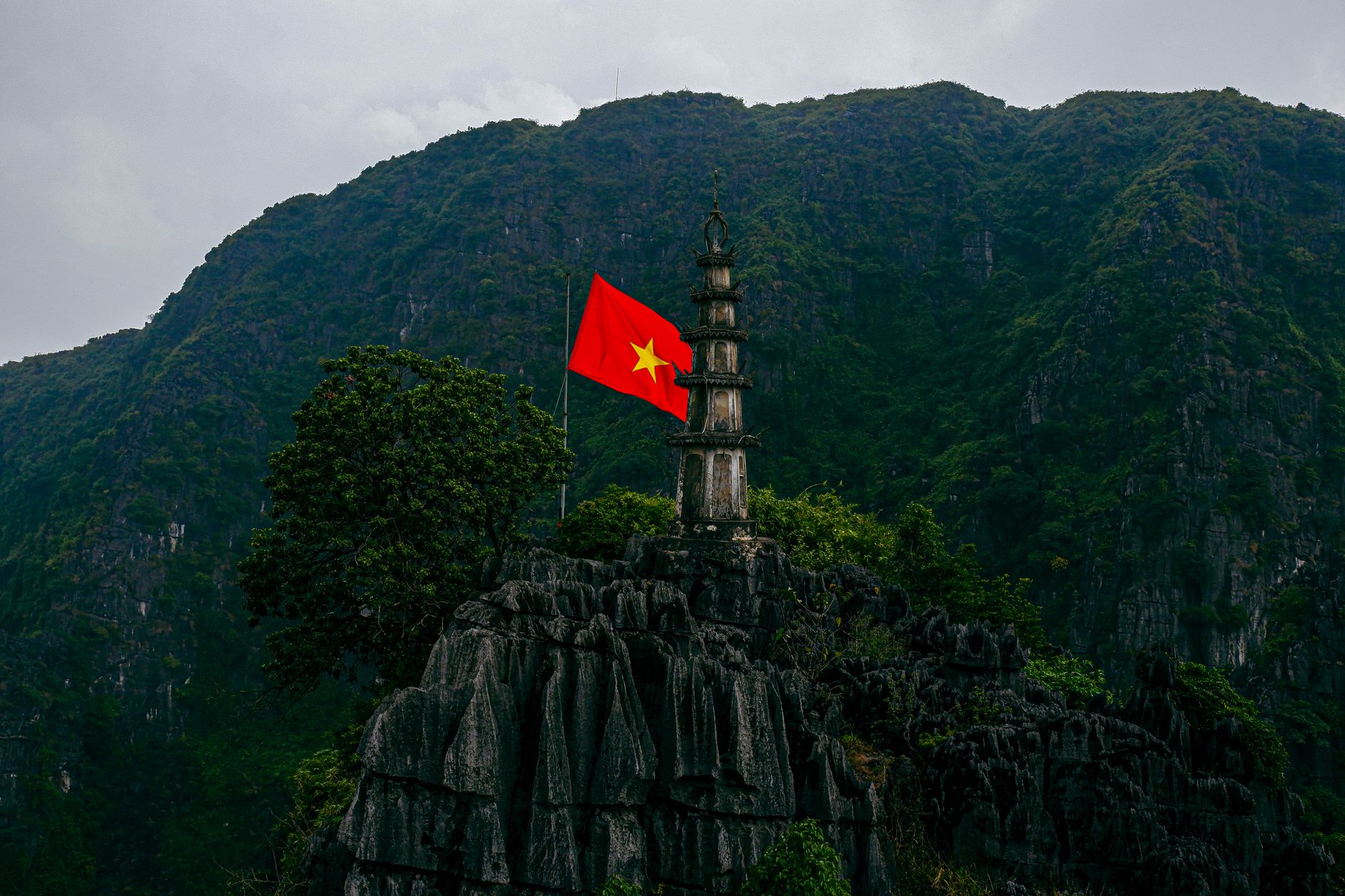 Scenic view of a pagoda and Vietnamese flag atop a mountain in Ninh Bình, Vietnam.