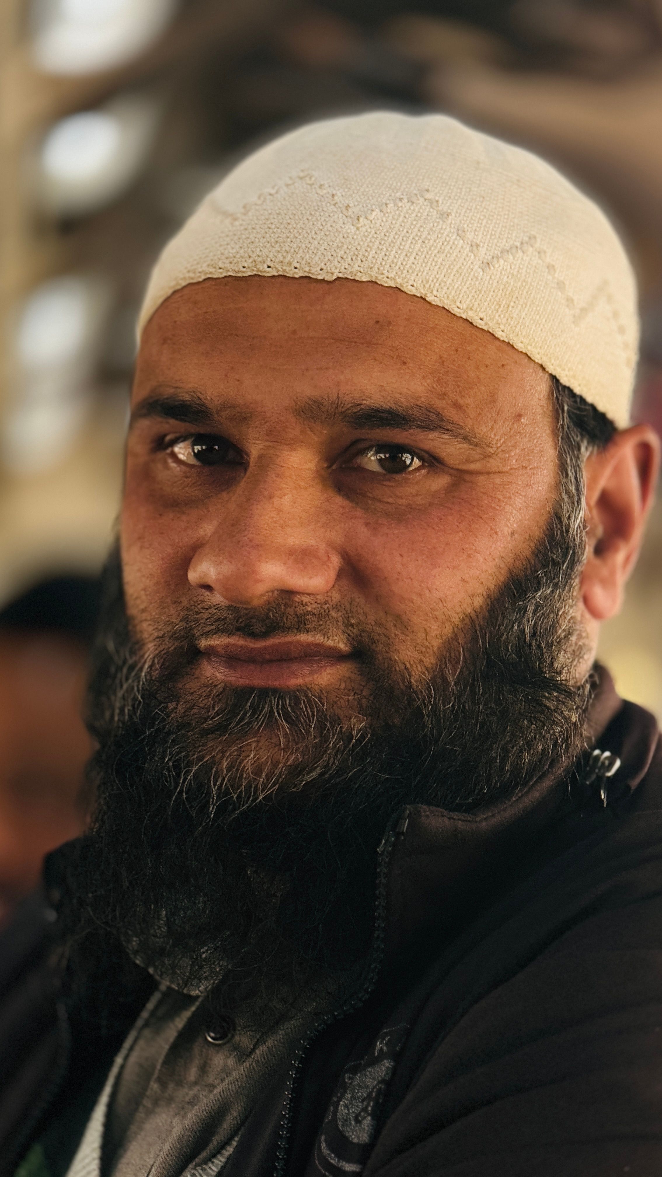 Close-up portrait of a senior man with a beard wearing a white cap.