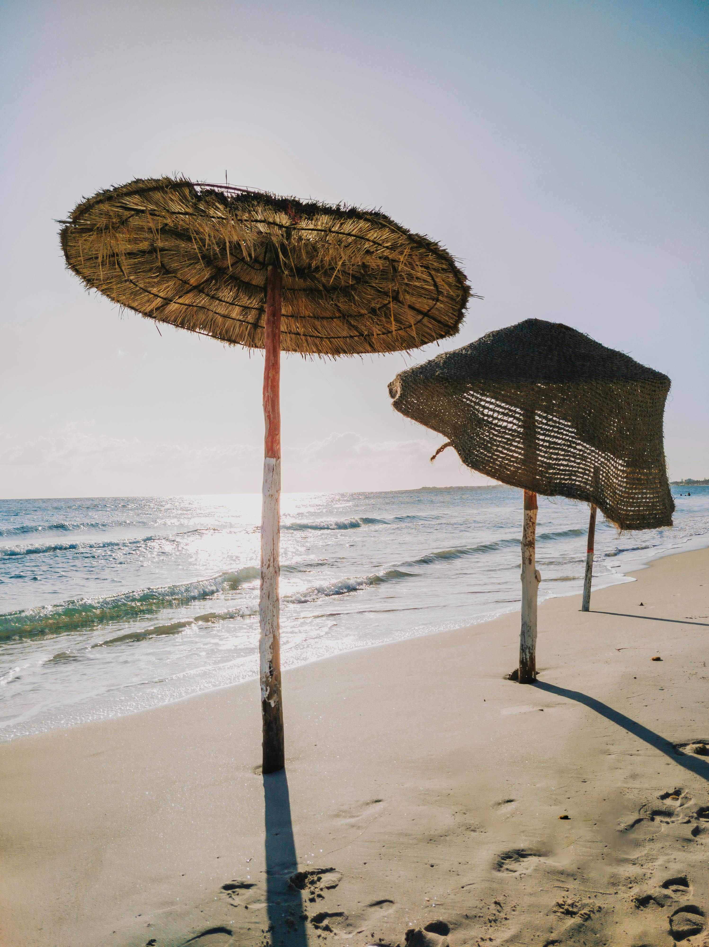 Serene sandy beach with straw umbrellas by the sea under a bright sunny sky.