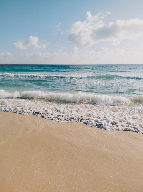 Free Relaxing ocean waves gently lapping on a sunlit sandy beach under a clear sky. Stock Photo