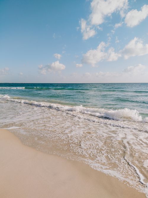 Free Tranquil beach with gentle waves under a clear sky, perfect for relaxation and escape. Stock Photo
