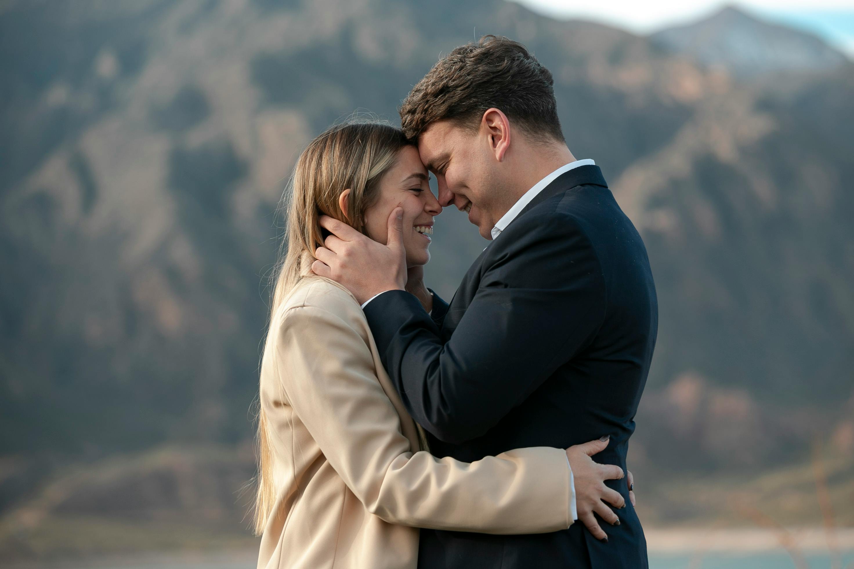 A loving couple embraces with mountains in the background, showcasing romance and connection.