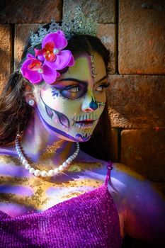 A woman with intricate Day of the Dead makeup and a floral accessory in vibrant colors.