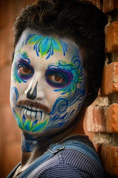 Vibrant creative makeup with floral patterns on a man's face against a brick background.