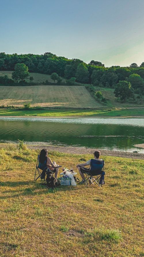 Free A couple enjoys a peaceful picnic beside a serene lake in summer. Stock Photo