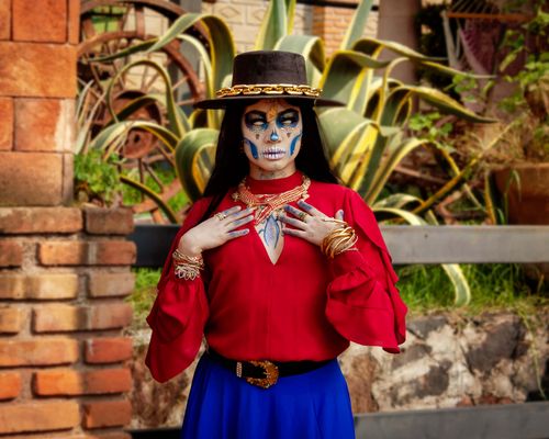 Free A woman dressed in Dia de Muertos makeup and costume stands outdoors in vibrant attire. Stock Photo