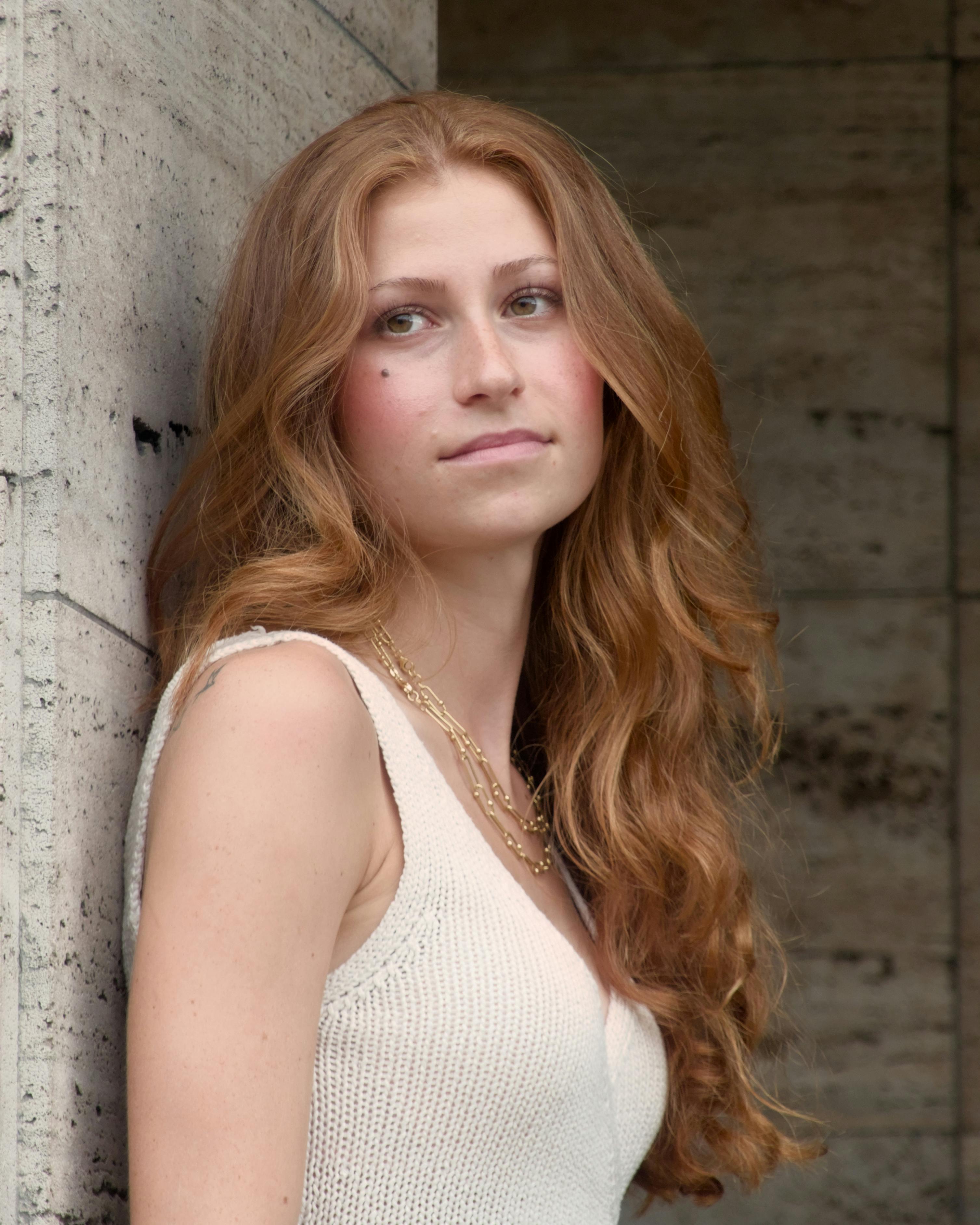 Elegant young woman with red hair in Berlin, wearing a white top and necklaces.