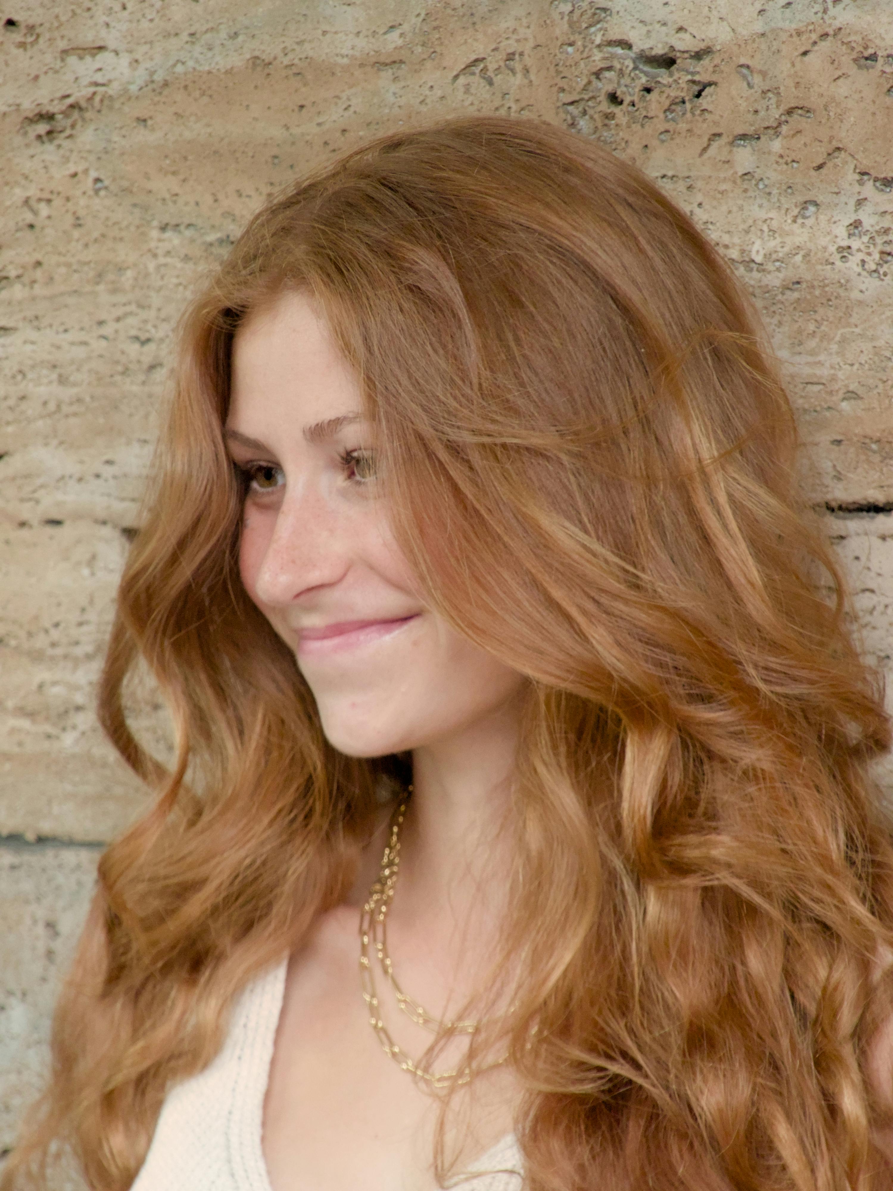 Close-up of a young redhead woman smiling against a stone wall in Berlin, Germany.