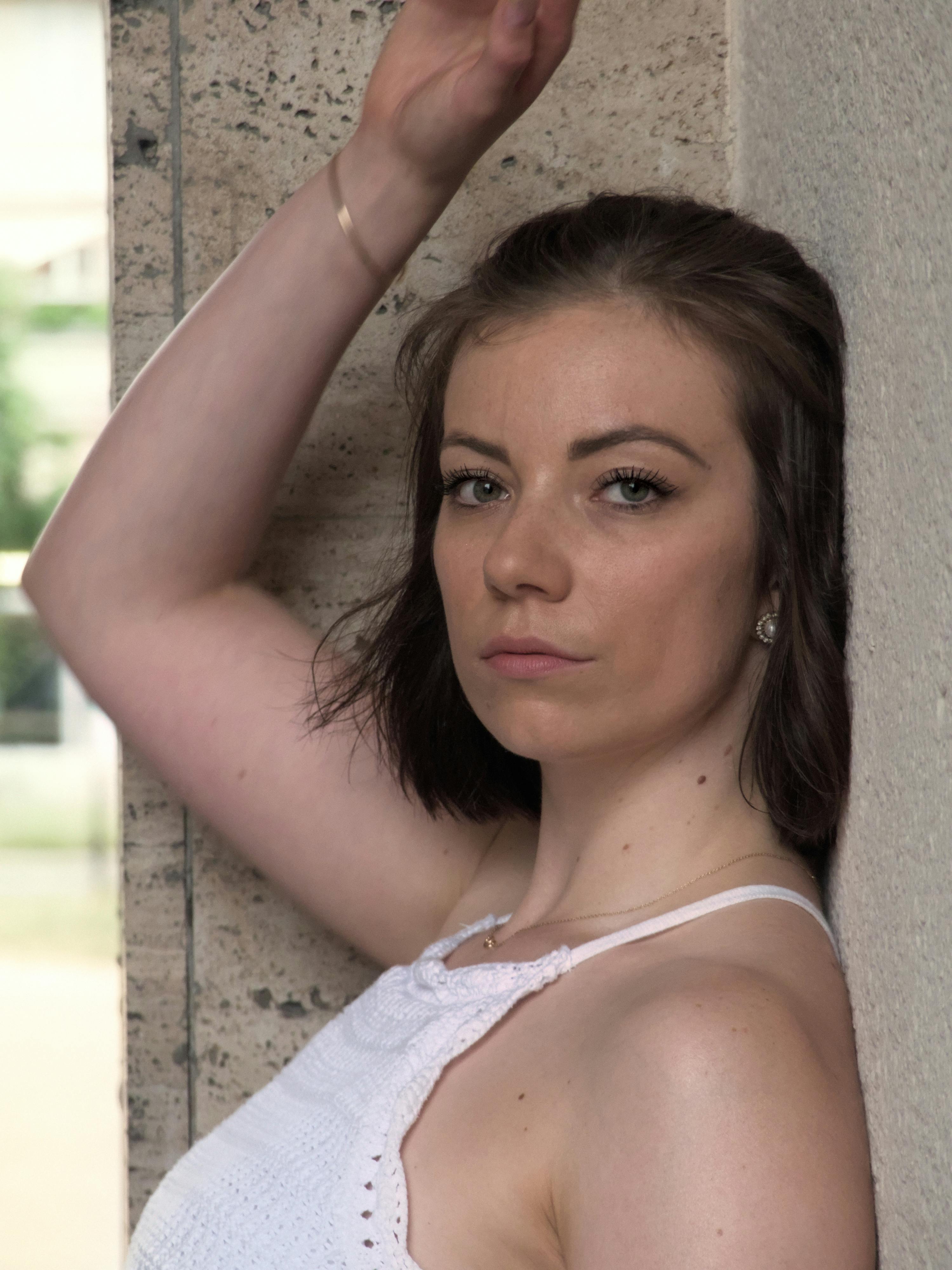 Portrait of a woman in a white blouse posing outdoors with urban background.