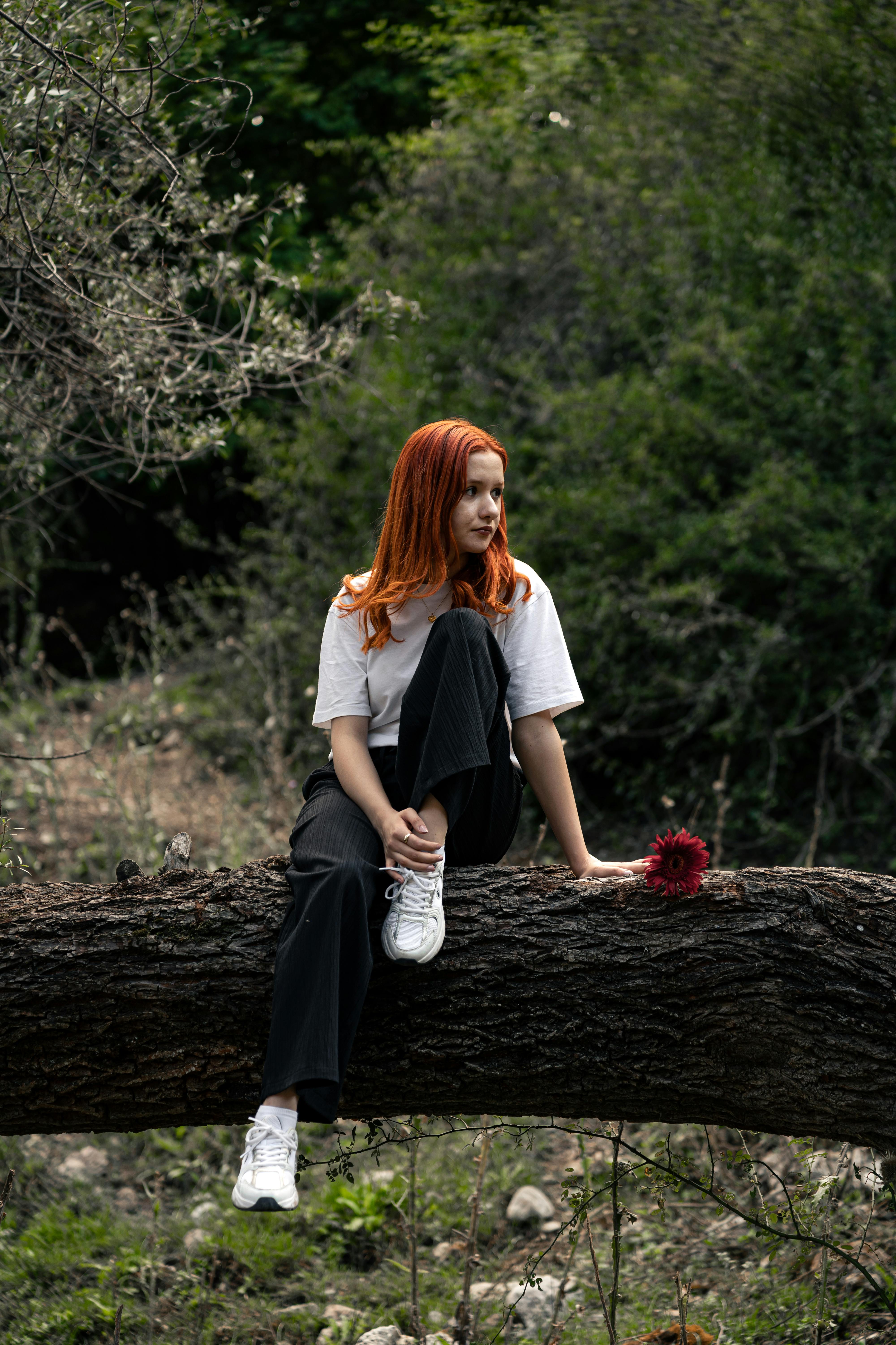 a woman with red hair sitting on a tree branch