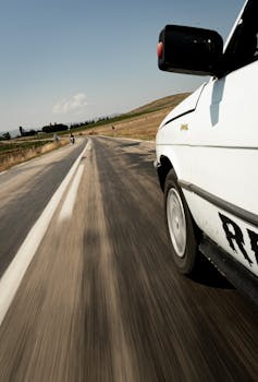 Motion capture of a car driving fast on a rural road with clear sky above.