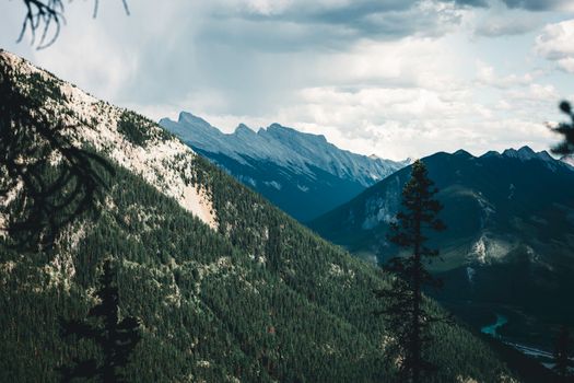 Stunning landscape of Banff's rocky mountains with lush forests under a cloudy sky.