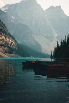 Serene view of canoes on Moraine Lake with majestic mountains in Banff National Park at dawn.